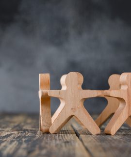 Business success and teamwork concept with wooden figures of people on wooden and foggy background side view.